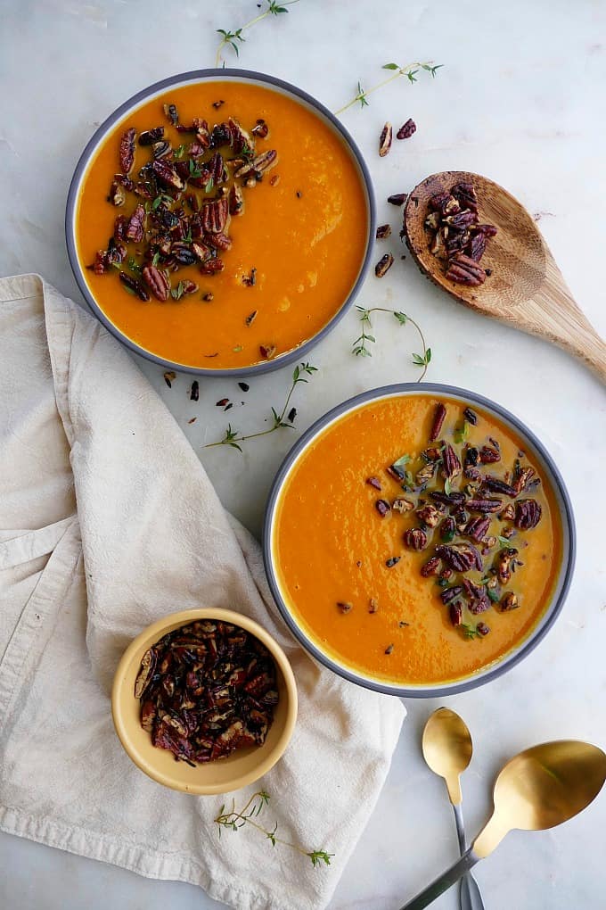 carrot and celery soup in two bowls with a small bowl of pecan crumble