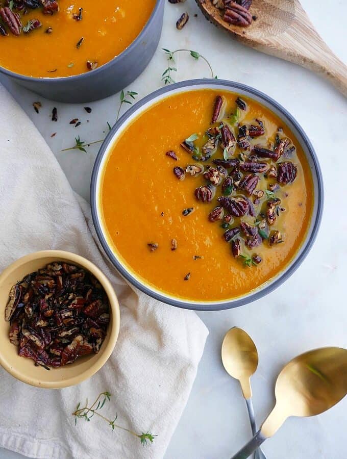 carrot and celery soup in one bowl with small bowl of pecan crumble