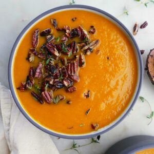 carrot and celery soup with thyme pecan crumble in a bowl on a white countertop