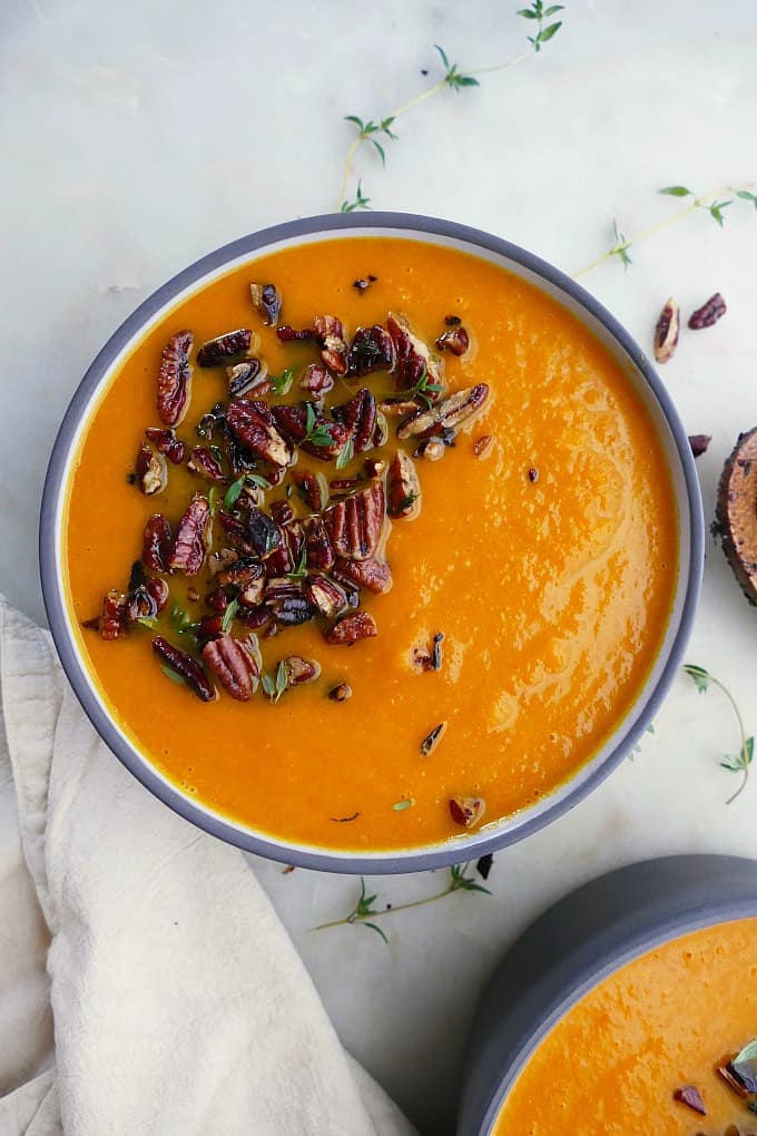 carrot and celery soup with thyme pecan crumble in a bowl on a white countertop