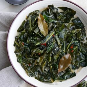 vegan collard greens in a white bowl topped with bay leaves