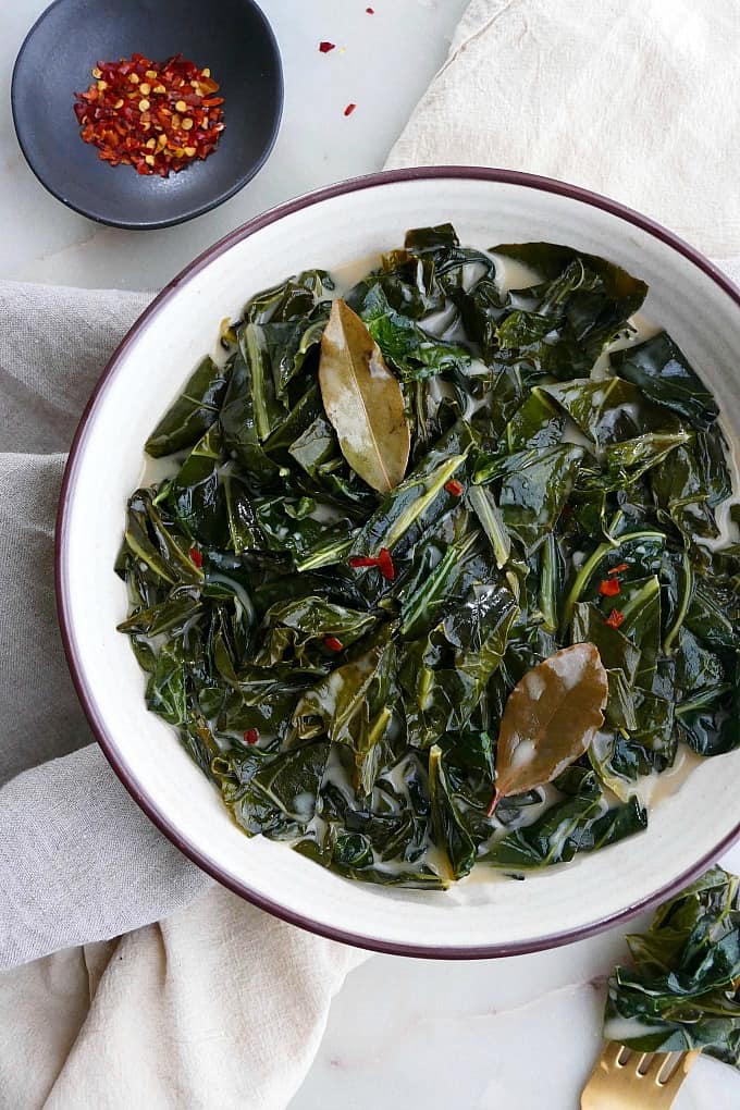 vegan collard greens in a white bowl topped with bay leaves