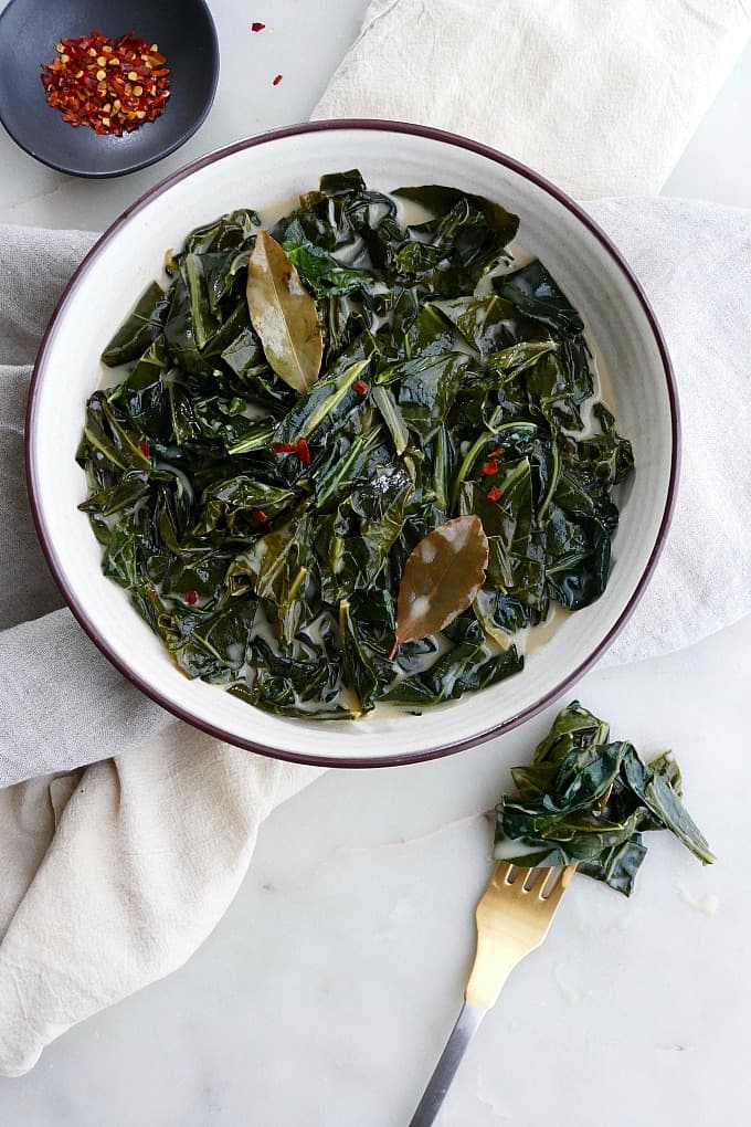 vegan collard greens in a white bowl with gold fork next to it