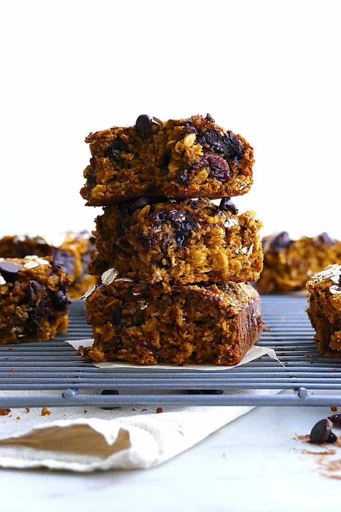 three pumpkin oatmeal bars in a stack on a wire cooling rack next to more bars