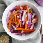 purple radish salad with carrots and green onions in a white bowl on top of a grey napkin