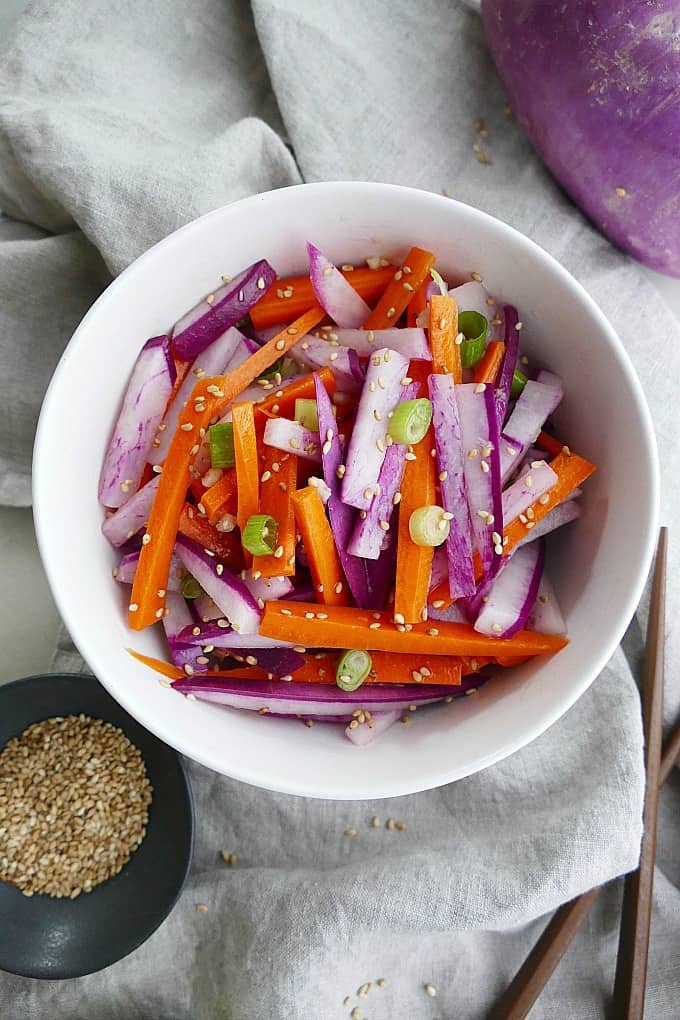 purple radish salad with carrots and green onions in a white bowl on top of a grey napkin