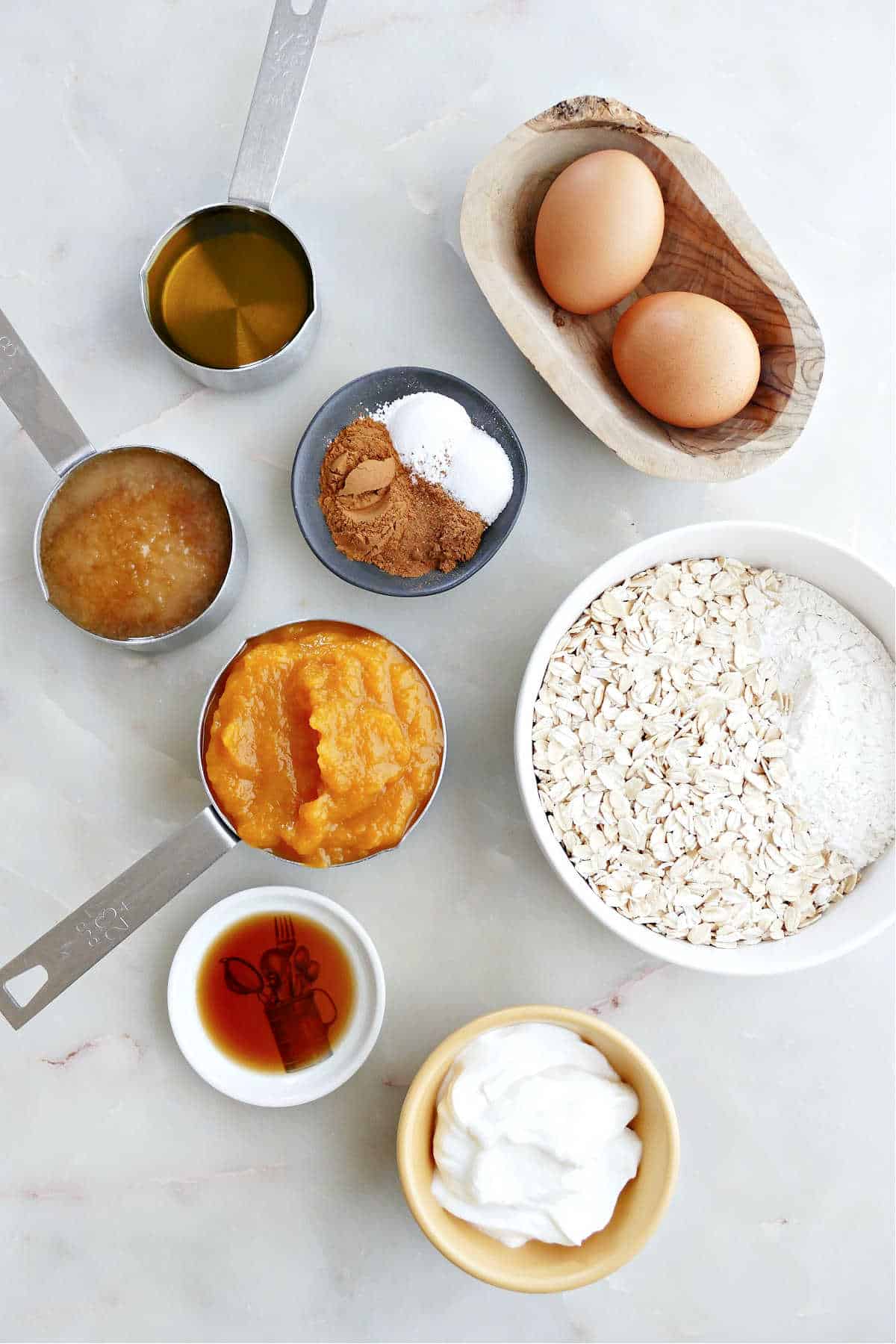 oats, flour, and spices in a bowl next to bowls with wet ingredients and eggs