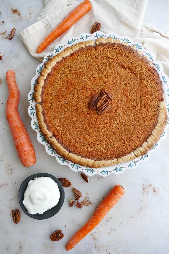 homemade carrot pie with pecans in the center next to carrots and whipped cream