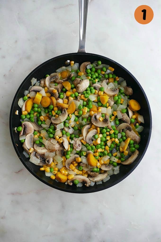 sauteed mushrooms, carrots, onions, peas, corn in a black skillet
