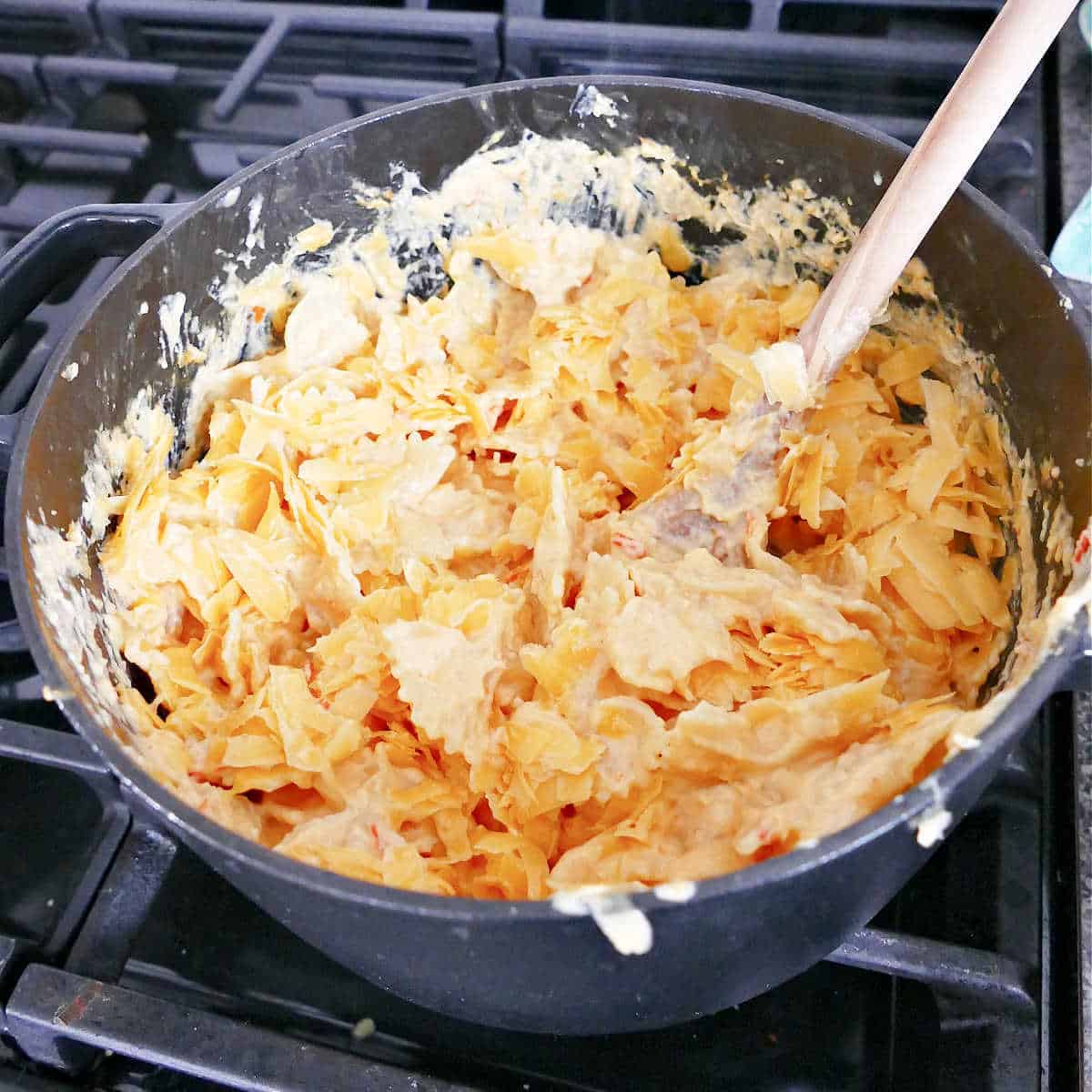 shredded cheddar cheese being folded into pasta in a pot