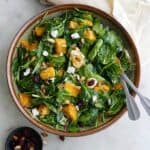 pumpkin salad in a large bowl with silver utensils on top of a yellow napkin