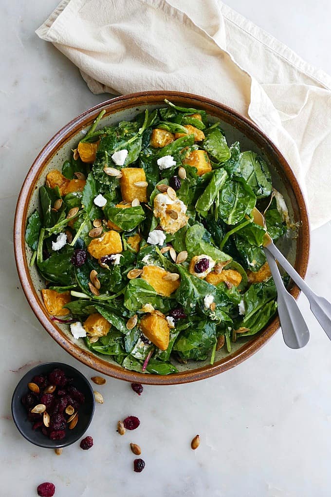 pumpkin salad in a large bowl with silver utensils on top of a yellow napkin