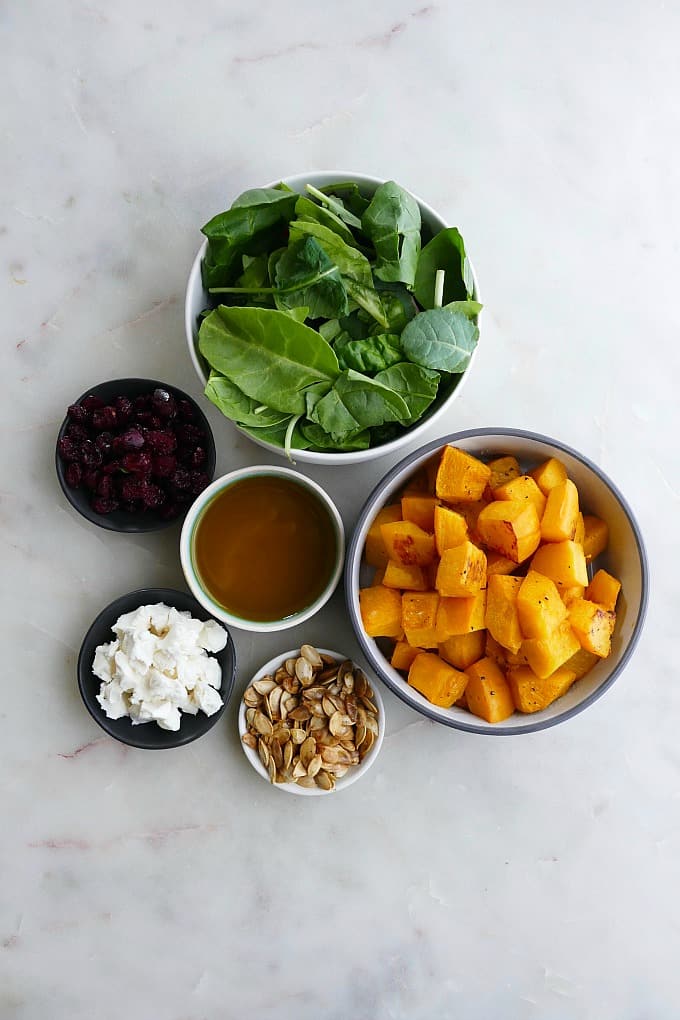 ingredients for roasted pumpkin salad in small bowls on a white countertop