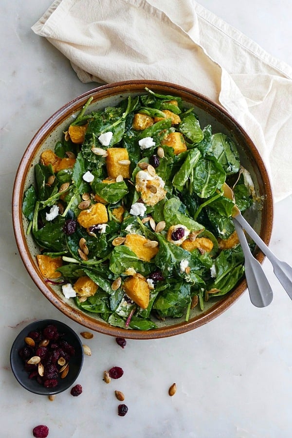 A bowl of roasted pumpkin salad with apple cider vinegar dressing on top and serving spoons. 