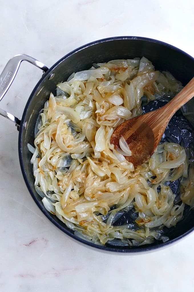 sauteed sweet onions in a black pot with a wooden spoon
