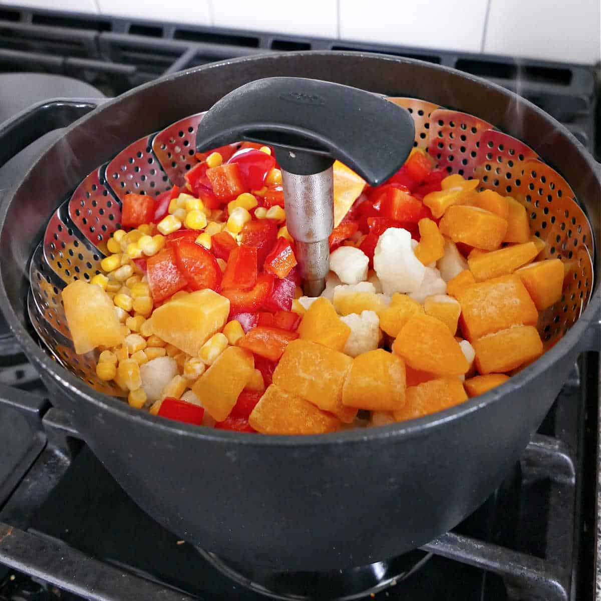 squash, cauliflower, peppers, and corn in a steamer basket in a pot