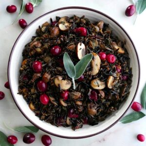 wild rice pilaf with mushrooms and cranberries in a white bowl topped with sage