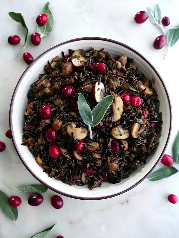 wild rice pilaf with mushrooms and cranberries in a white bowl topped with sage