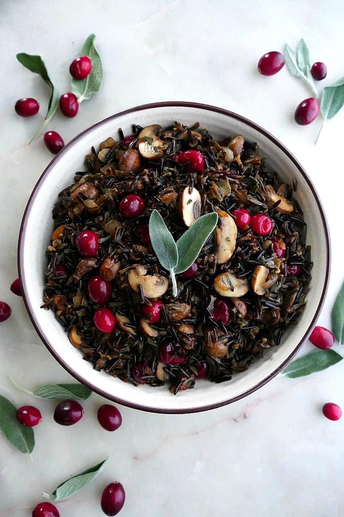 wild rice pilaf with mushrooms and cranberries in a white bowl topped with sage