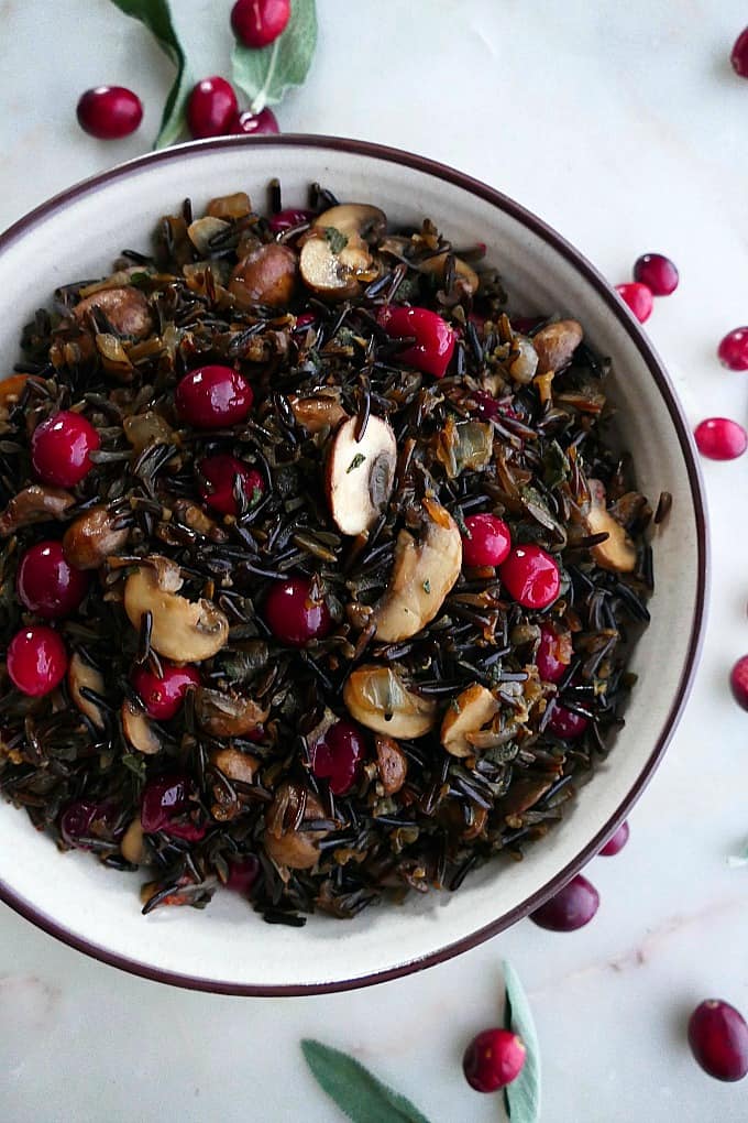 close up of wild rice pilaf with mushrooms and cranberries in a white bowl