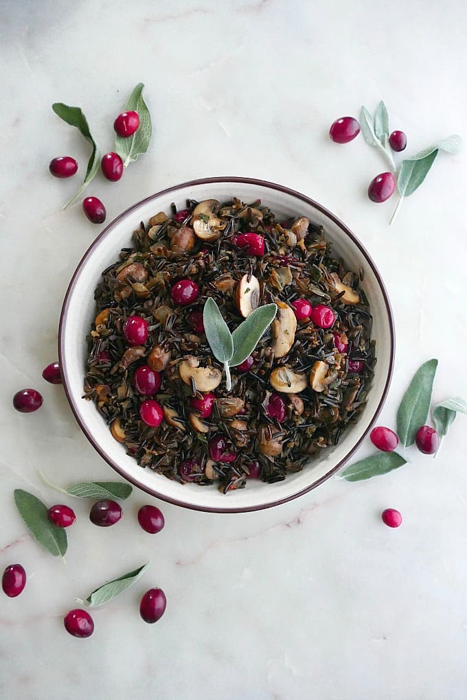 wild rice pilaf with mushrooms and cranberries in a white bowl topped with sage