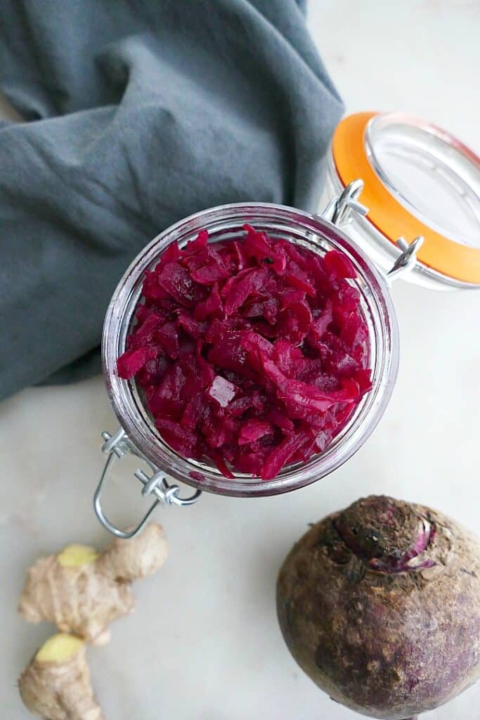 close up of homemade beetroot relish in a glass jar next to a blue napkin