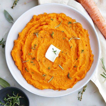 carrot and swede mash on a white plate with a slab of butter in the center