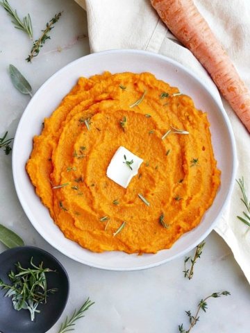 carrot and swede mash on a white plate with a slab of butter in the center