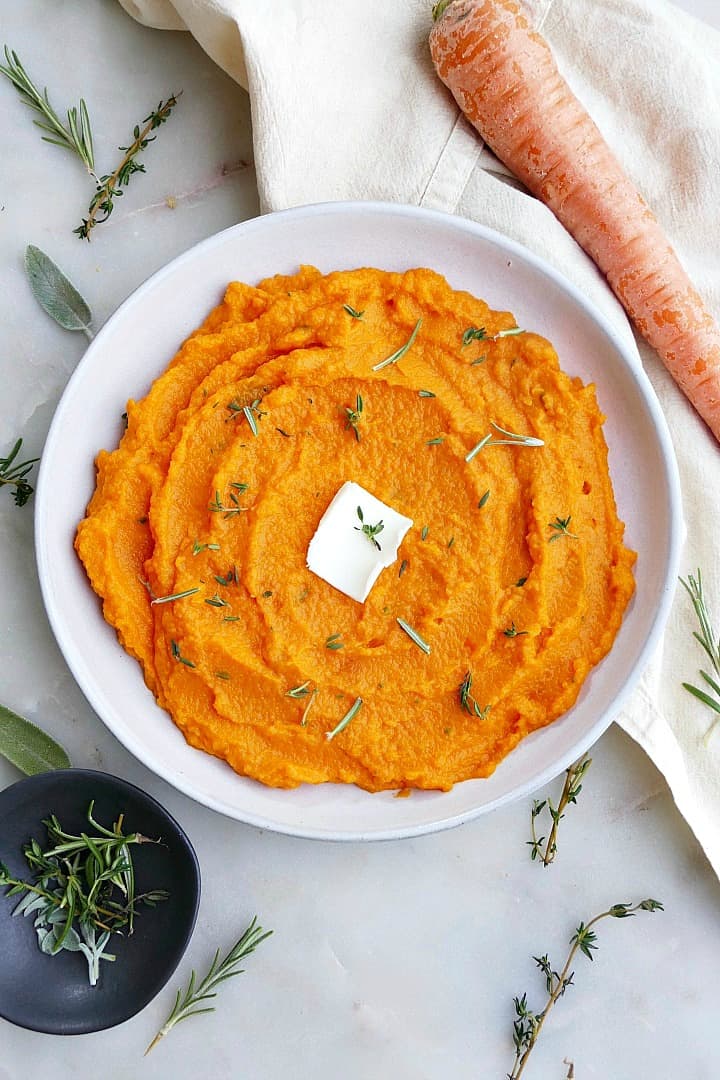 carrot and swede mash on a white plate with a slab of butter in the center