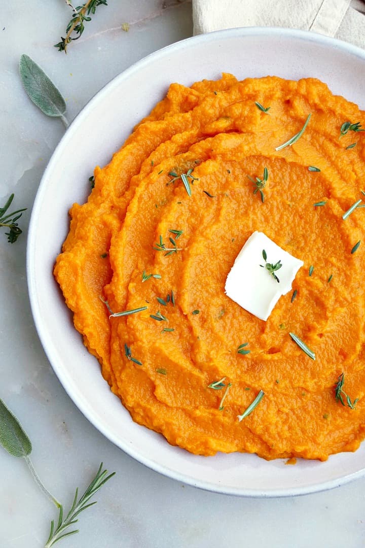 close up of carrot and swede mash on a white plate with butter and herbs