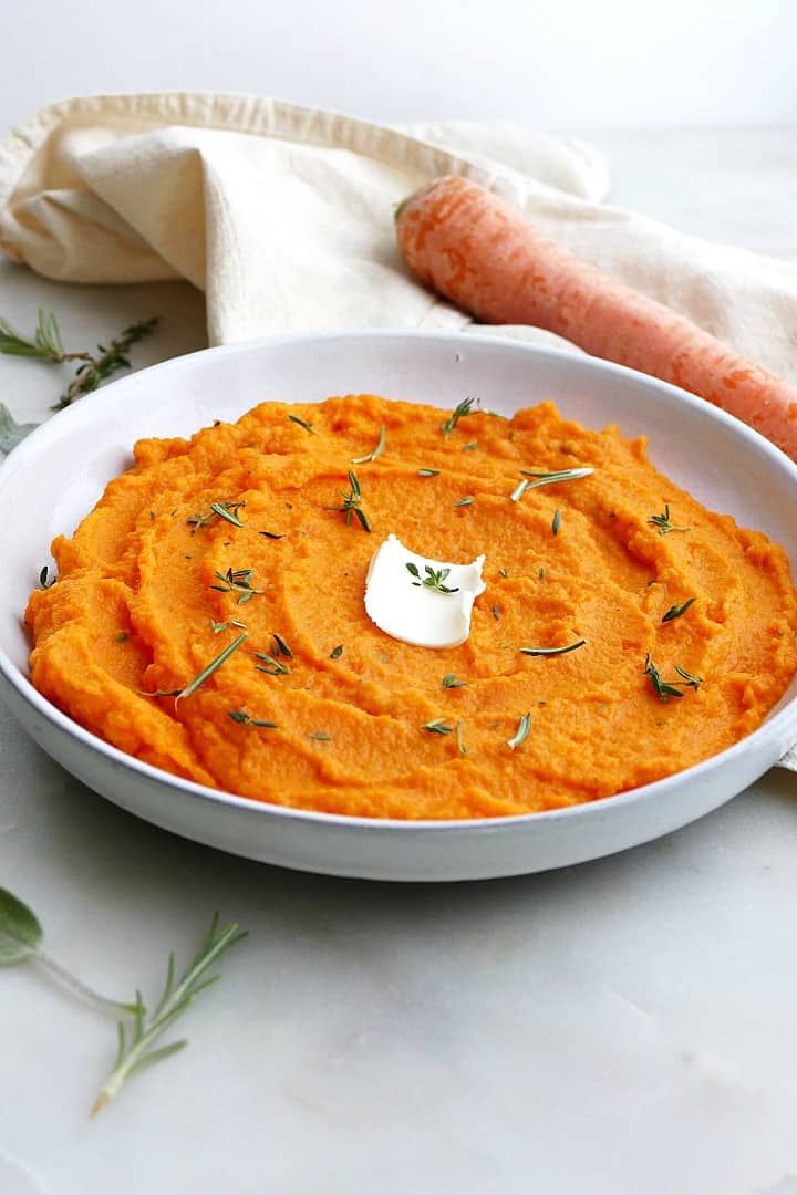 side view of carrot and swede mash on a white plate with butter and herbs