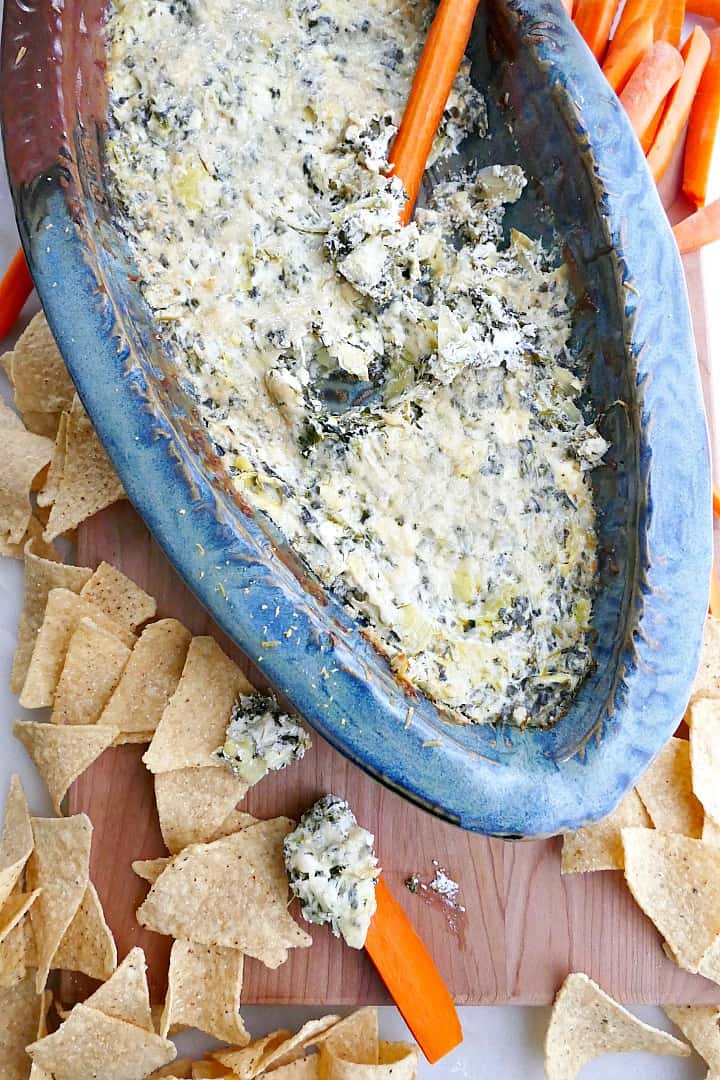 close up of spinach artichoke dip on a wooden board with chips and carrots