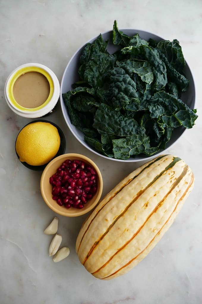 bowl of kale, delicata squash, tahini, pomegranate arils, lemon, and garlic on a white counter