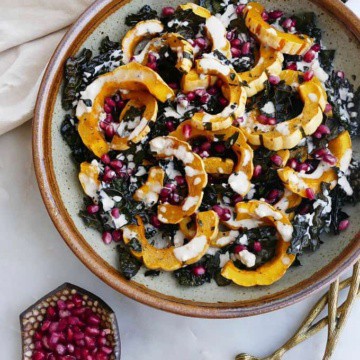 green and brown bowl with roasted delicata squash on a counter next to gold utensils