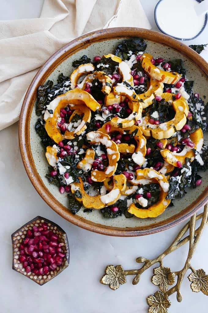 green and brown bowl with roasted delicata squash on a counter next to gold utensils