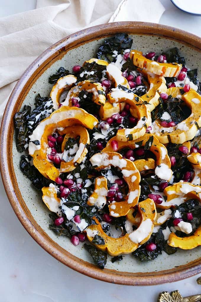 close up of roasted delicata squash and kale in a bowl with pomegranate seeds and dressing