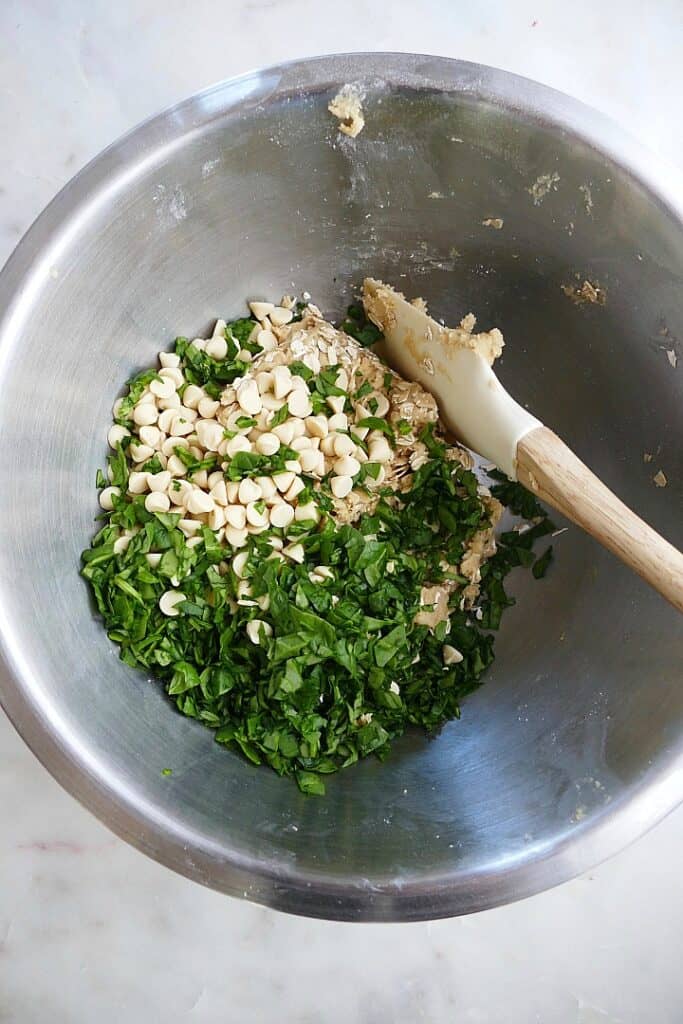 batter for spinach white chocolate chip oat cookies in a mixing bowl with spatula