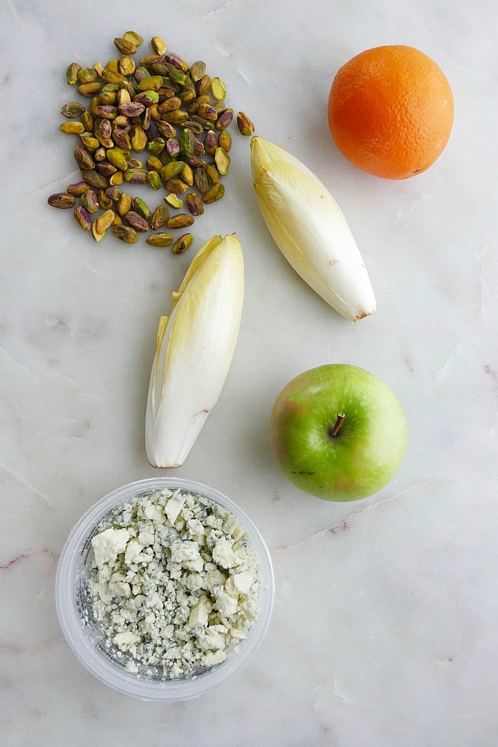 pistachios, belgian endive, orange, granny smith apple, and blue cheese on a counter