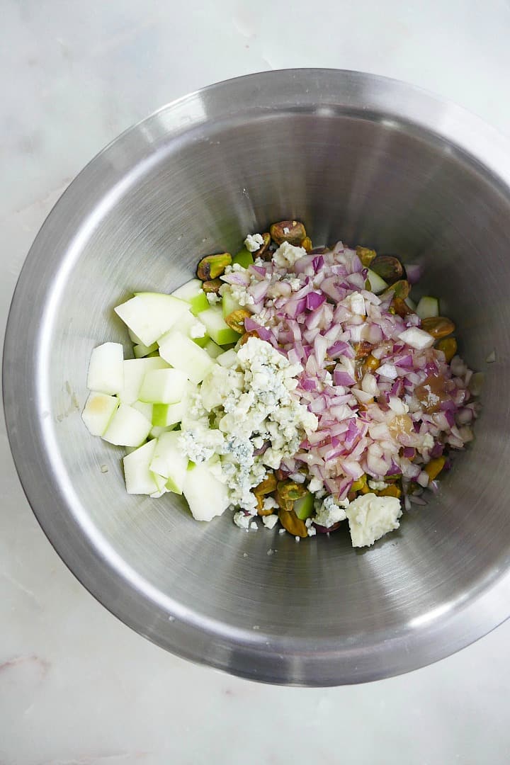 diced apples, shallots, pistachios, and blue cheese in a silver mixing bowl