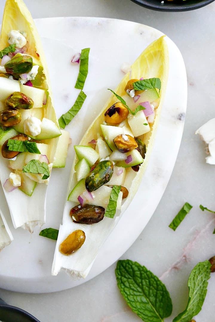 close up of stuffed belgian endive with apple, blue cheese, pistachios, and mint