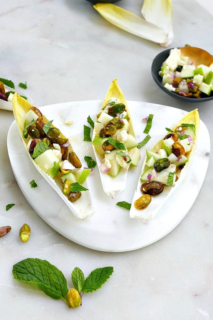 side view of three stuffed endive leaves on a marble plate on a countertop