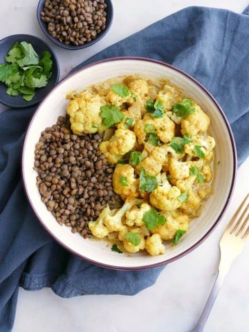 cauliflower curry with lentils in a white bowl on a blue napkin