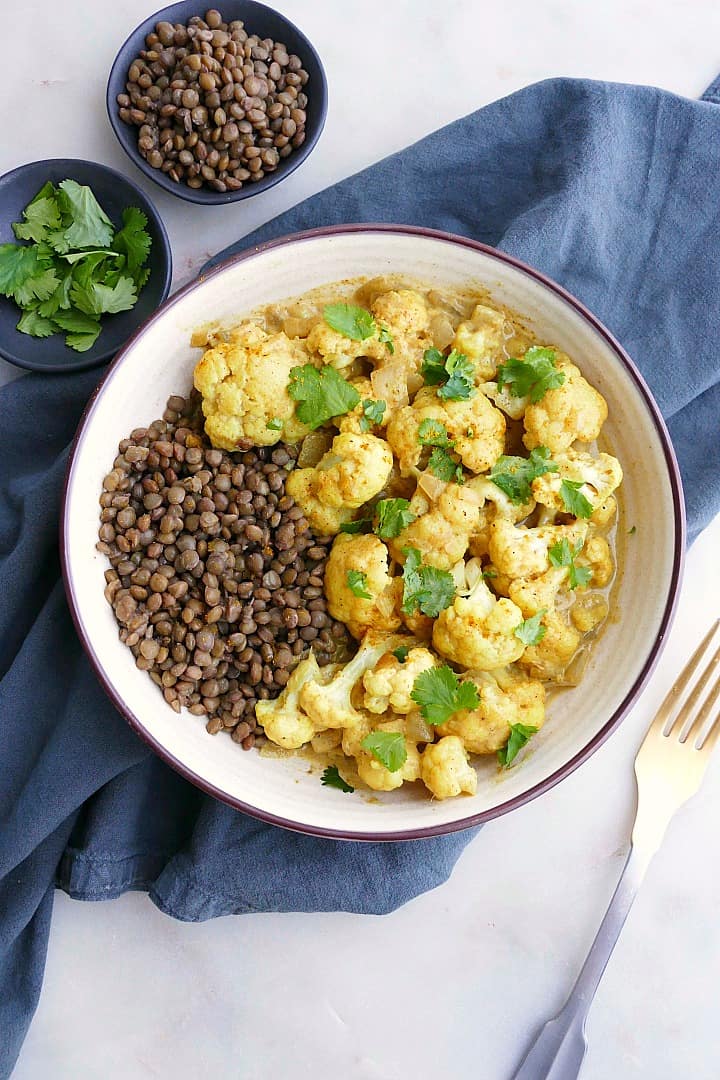 cauliflower curry with lentils and cilantro in a white bowl on a blue napkin