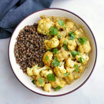 cauliflower curry with lentils and cilantro in a white bowl on a white counter