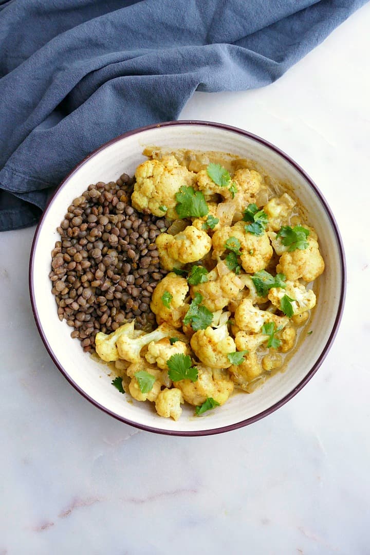 cauliflower curry with lentils and cilantro in a white bowl on a white counter