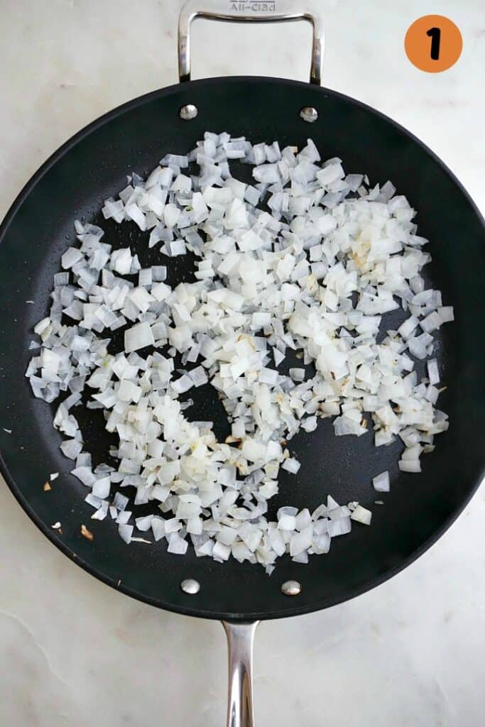 diced white onion with coconut oil cooking in a black skillet