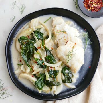 coconut poached cod with fennel and spinach on a black plate on a napkin