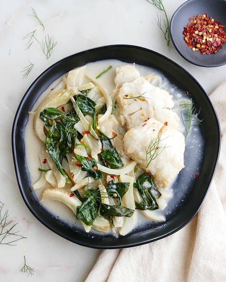 coconut poached cod with fennel and spinach on a black plate on a napkin