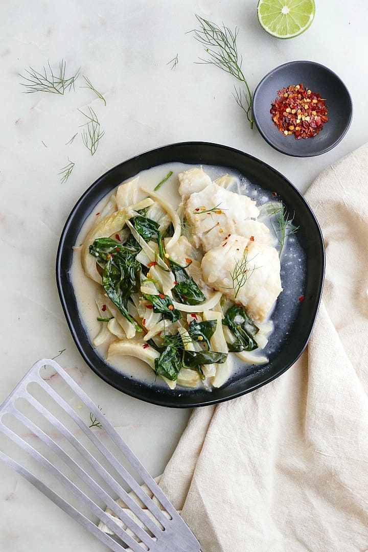 coconut cod with fennel and spinach on a black plate on a white counter