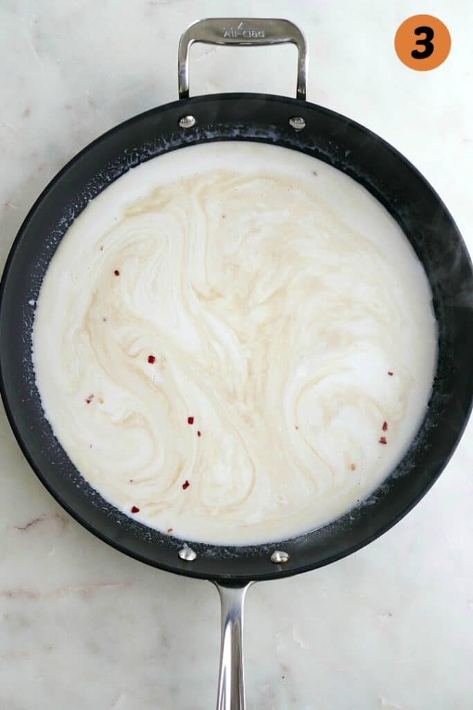 coconut milk, soy sauce, and red pepper in a black skillet on a white counter